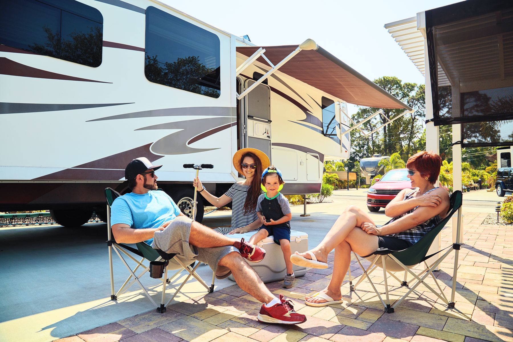 A family relaxing in camp chairs under an RV awning